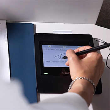 Eine weibliche Hand unterzeichnet etwas auf einem Signature-Tablet. 