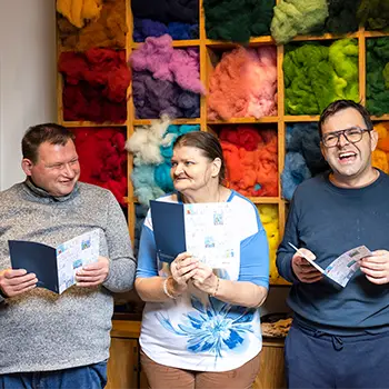 Zwei Männer und eine Frau stehen vor einem Regal und halten jeweils ein Heft in den Händen.