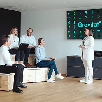 Eine Gruppe von Personen sitzen vor einer Frau, die vor ein Bildschirm etwas präsentiert. 